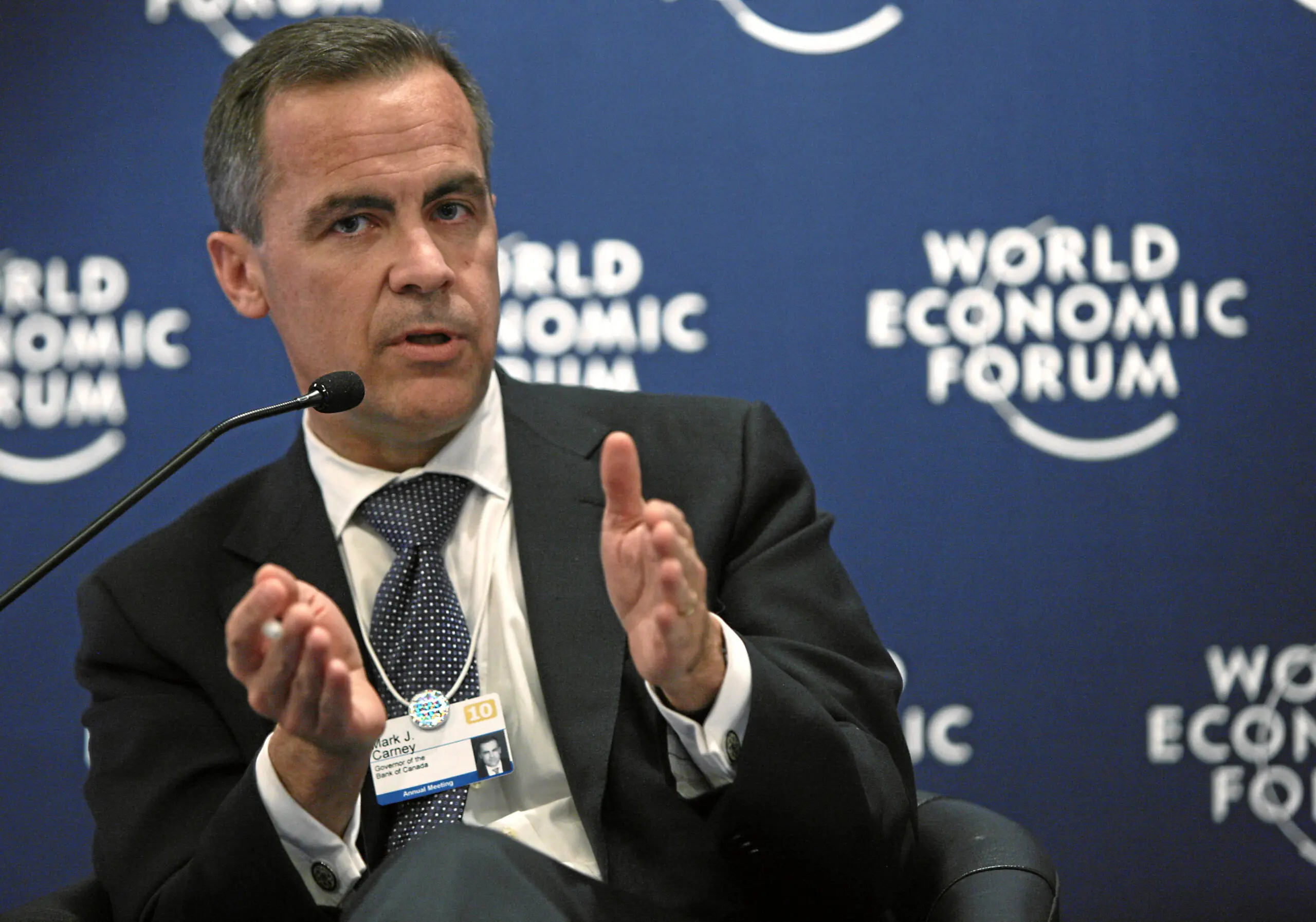 Mark Carney en costume s'adressant à un public à l'extérieur, arrière-plan flou suggérant un lieu hi